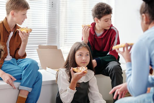 Group of teenagers enjoying pizza indoors, having fun in a relaxed, social setting.